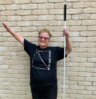 Tricia Waechter holding her white cane in one hand wearing a Blind Girl Designs t-shirt.
