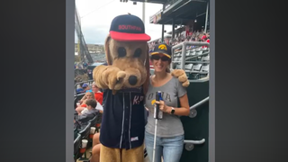 Adriann Keven with her white cane standing with a dog baseball mascot.