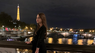 Evening photo of Marwa Ibrahim standing on a bridge overlooking the Seine River in Paris with the Eiffel Tower in the background.