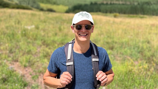 Steven Ringel with a backpack on, hiking through a valley with a blurred mountain in the background.