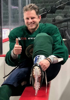 Shawn Hewson putting on his hockey gear and ice skates giving a thumbs up.